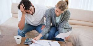 A married couple looking distressed on the couch while examining finances with a calculator, hinting at financial infidelity issues.