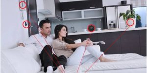 Husband and wife in living room, surrounded by spy recording device. 